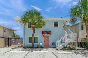 A two-story building with a red awning, a staircase, and a palm tree in the foreground. - Siesta Key Base | Walk to Beach | Free Activities (Sarasota)