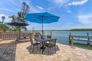 An outdoor patio with a table and chairs, two umbrellas, and a view of a lake. - Siesta Key Base | Walk to Beach | Free Activities (Sarasota)