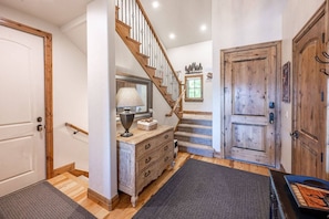 A staircase leading to a second floor, a wooden door, a dresser with drawers, a lamp, and a rug.
