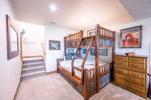 A bedroom with a bunk bed, a wooden dresser, and a staircase.
