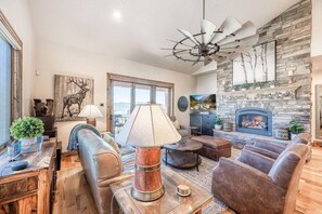A spacious living room with a fireplace, leather sofas, a coffee table, and a large window.