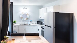 Una cocina moderna con armarios blancos, un refrigerador negro, un microondas y un lavamanos.