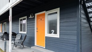 Una casa con una puerta de color naranja brillante, dos ventanas y un porche con sillas.