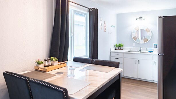 Una cocina moderna con armarios blancos, un lavamanos y un ventanal con cortinas oscuras.
