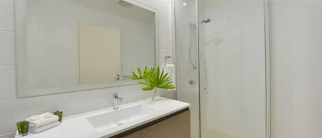Un baño moderno con cabina de ducha de vidrio, un lavabo blanco y un espejo grande.