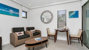 A modern living room with a wicker sofa, two chairs, a round table, and a mirror on the wall. - Seascape Holidays at Seascape Temple - Studio (Douglas)