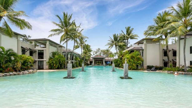 A resort pool with clear water, surrounded by palm trees and modern buildings. - Seascape Holidays at Seascape Temple - Studio (Douglas)