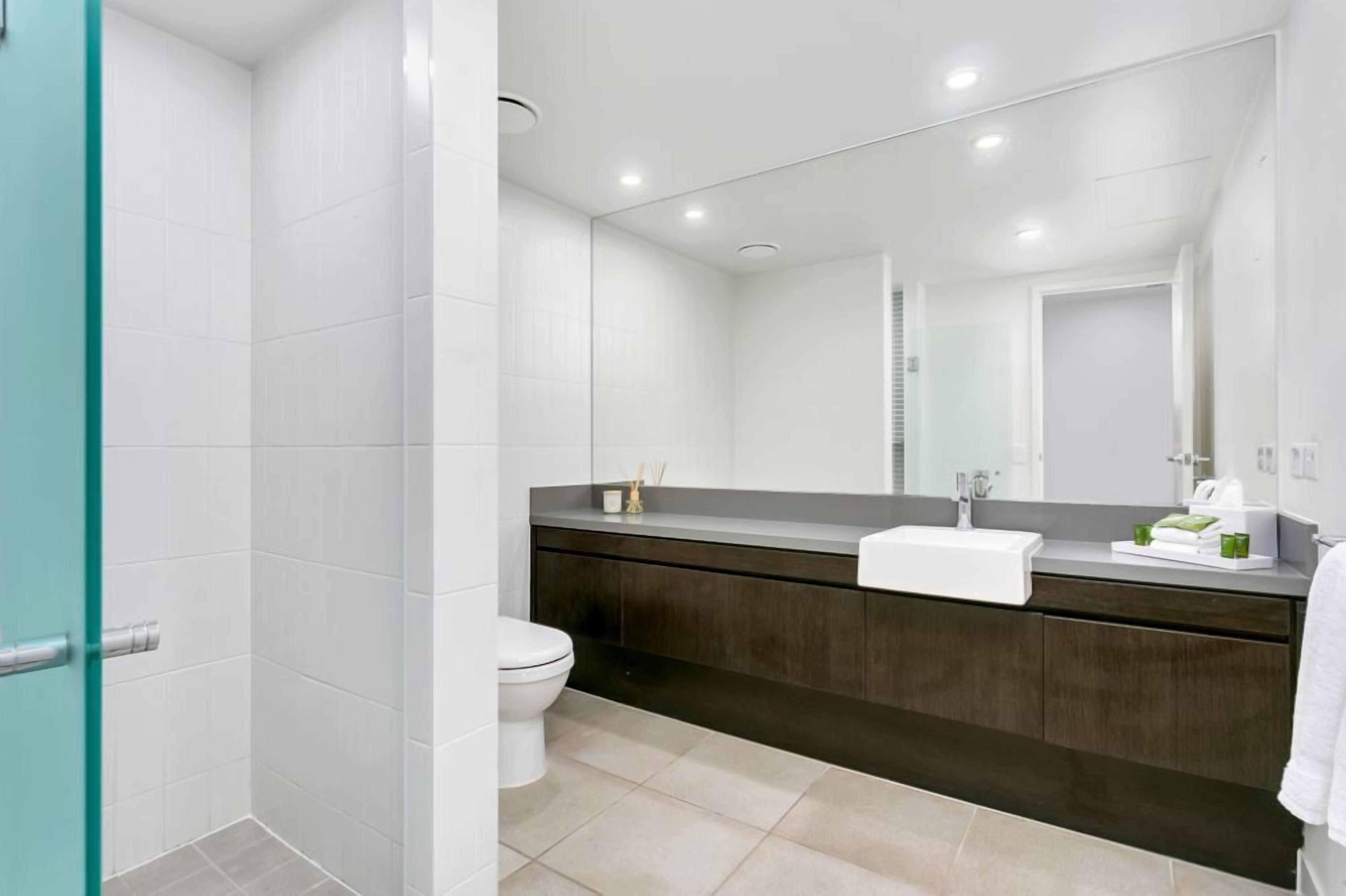 Een moderne badkamer met een wit toilet, een donker houten wastafelmeubel en een grote spiegel.