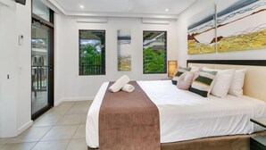 Une chambre moderne avec un grand lit, un ventilateur de plafond et une vue sur la verdure par les fenêtres.