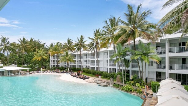 Ein Resort mit Pool, Palmen und einem weißen Gebäude mit Balkonen.