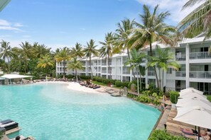Un complexe hôtelier doté d’une piscine, de palmiers et d’un bâtiment blanc agrémenté de balcons.