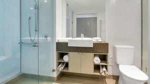 Ein modernes Badezimmer mit einer in Glas abgeschirmten Dusche, einem weißen Waschbecken mit Marmorplatte und einer Toilette.