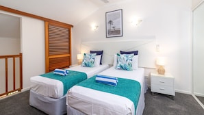 Habitación de hotel con dos camas, un ventilador de techo, un cuadro en la pared y una mesita de noche con lámpara.