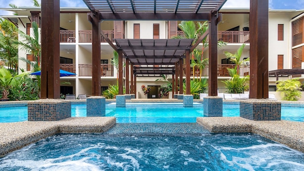 Un área de piscina de hotel con un jacuzzi, sillones de descanso y un espacio de estar techado.