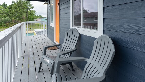 A wooden deck with two Adirondack chairs, a white railing, and a house with blue siding and a window. - AquaShores#3 - Pet friendly, BBQ grill & free Wifi (Ocean Shores)