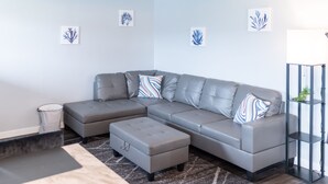 A modern living room with a grey sectional sofa, a patterned ottoman, and a geometric rug. - AquaShores#3 - Pet friendly, BBQ grill & free Wifi (Ocean Shores)