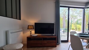 Uma sala de estar moderna com uma televisão de tela plana sobre um suporte de madeira, um banquinho de vime e uma mesa de jantar com cadeiras.