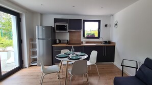 Cozinha compacta com eletrodomésticos modernos, sala de jantar com mesa e cadeiras, e um sofá.