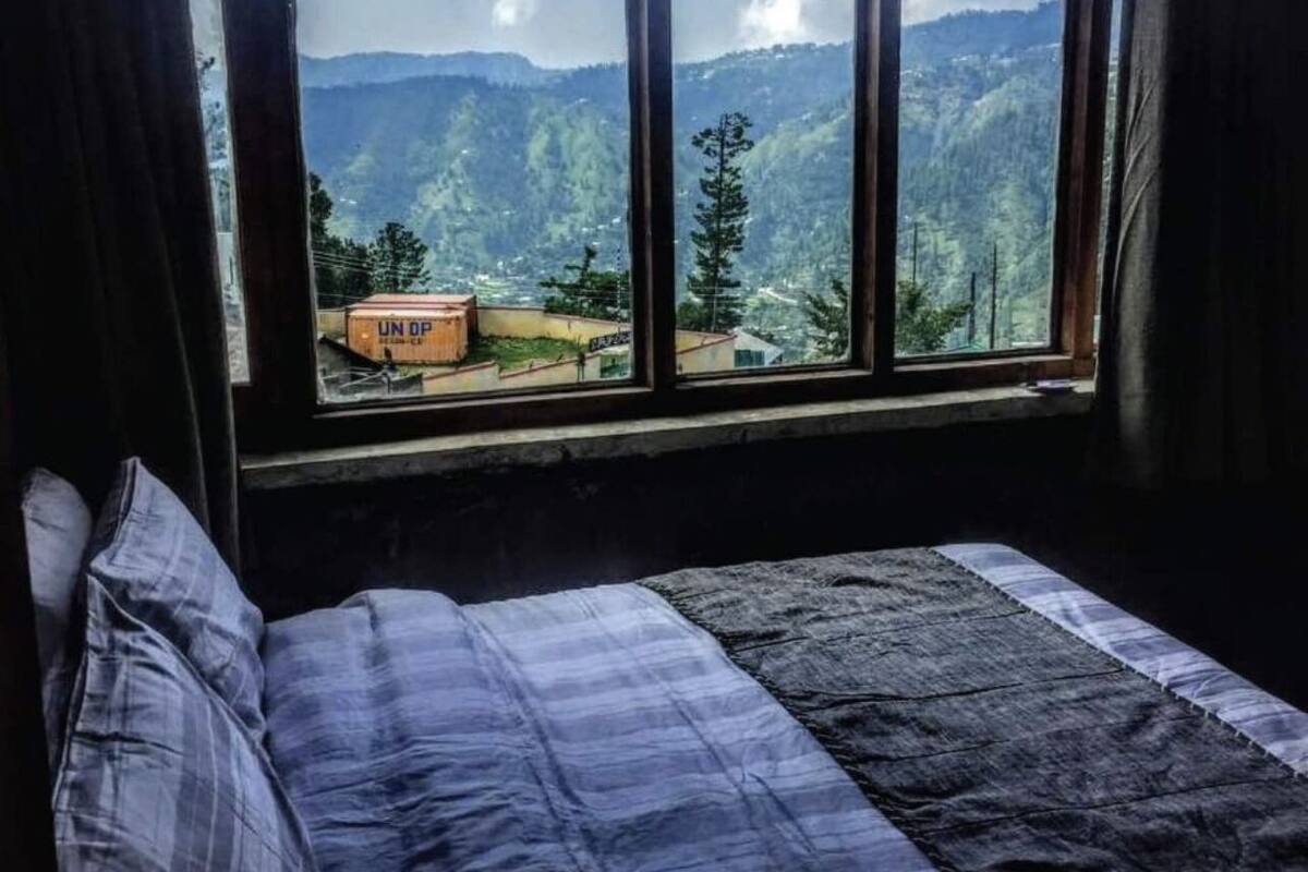 A room with a bed, a window, and a view of a mountainous landscape.