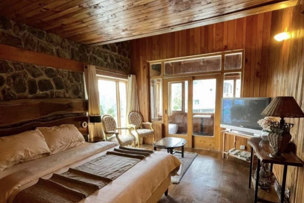 A bedroom with a large bed, a stone wall, wooden ceiling, and a TV.