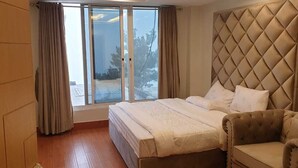 A bedroom with a large bed, a cushioned headboard, a sofa, and a sliding glass door leading to a snowy outdoor area. - Orangeloft Kalabagh (Abbottabad)
