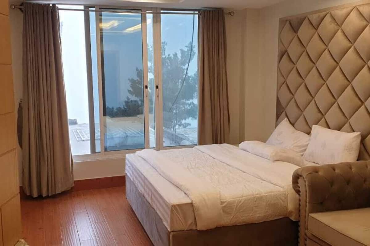 Ein Schlafzimmer mit einem großen Bett, einem gepolsterten Kopfteil, einer Sitzecke und einer Glastür, die zu einer verschneiten Außenanlage führt.