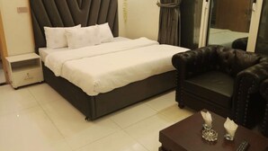 A bedroom with a bed, a nightstand, a leather sofa, and a small table with a remote control. - Orangeloft Kalabagh (Abbottabad)