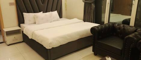 A bedroom with a bed, a nightstand, a leather sofa, and a small table with a remote control.