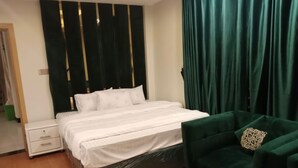 A bedroom with a bed, a nightstand, a green armchair, and a curtain. - Orangeloft Kalabagh (Abbottabad)