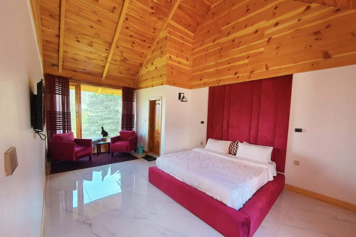 Un dormitorio espacioso con una cama grande, techo de madera y vistas al verdor exterior.