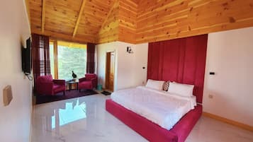 A spacious bedroom with a large bed, wooden ceiling, and a view of greenery outside.