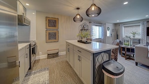 A modern kitchen with a central island, pendant lighting, and a dining area with a sofa and table. -  Luxury Town Square Condo king Bed & W/D (Blairsville)
