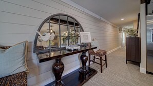 A hallway with a mirrored wall, a dark wooden console table, and a chair. -  Luxury Town Square Condo king Bed & W/D (Blairsville)