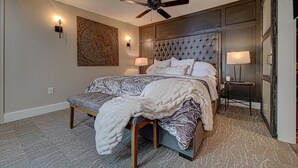 A bedroom with a large bed, a ceiling fan, a wall-mounted light, and a decorative wall piece. -  Luxury Town Square Condo king Bed & W/D (Blairsville)