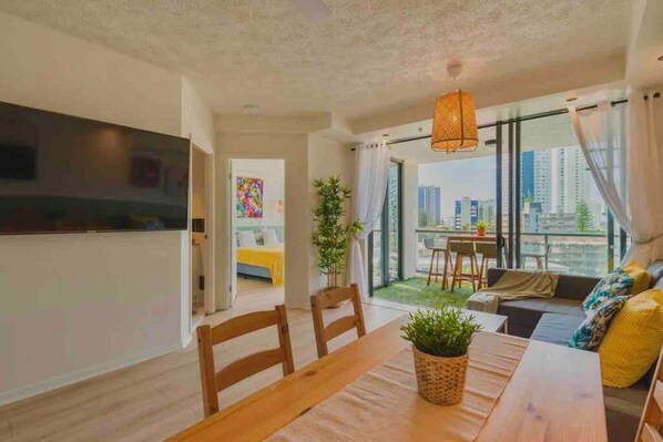 A modern living room with a dining area, large windows, and a view of the cityscape.