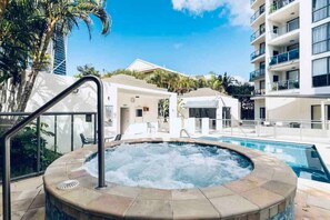 A hotel pool area with a hot tub, lounge chairs, and a building in the background.