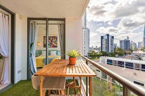 A balcony with a wooden table, a potted plant, and a view of a cityscape with tall buildings.