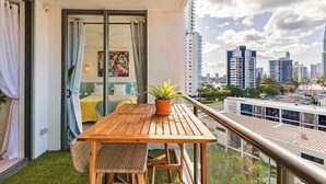 A balcony with a wooden table and chairs, a potted plant, and a city view. - New Modern Deco' Apartment - Ocean View (Surfers Paradise)