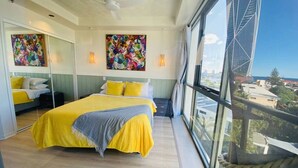 A modern bedroom with a large bed, a mirror, and a view of the city through large windows. - New Modern Deco' Apartment - Ocean View (Surfers Paradise)