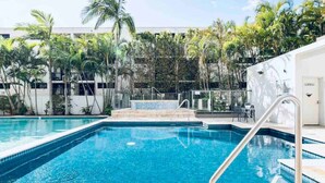 A rectangular swimming pool with a tiled edge, surrounded by palm trees and a white building in the background. - New Modern Deco' Apartment - Ocean View (Surfers Paradise)