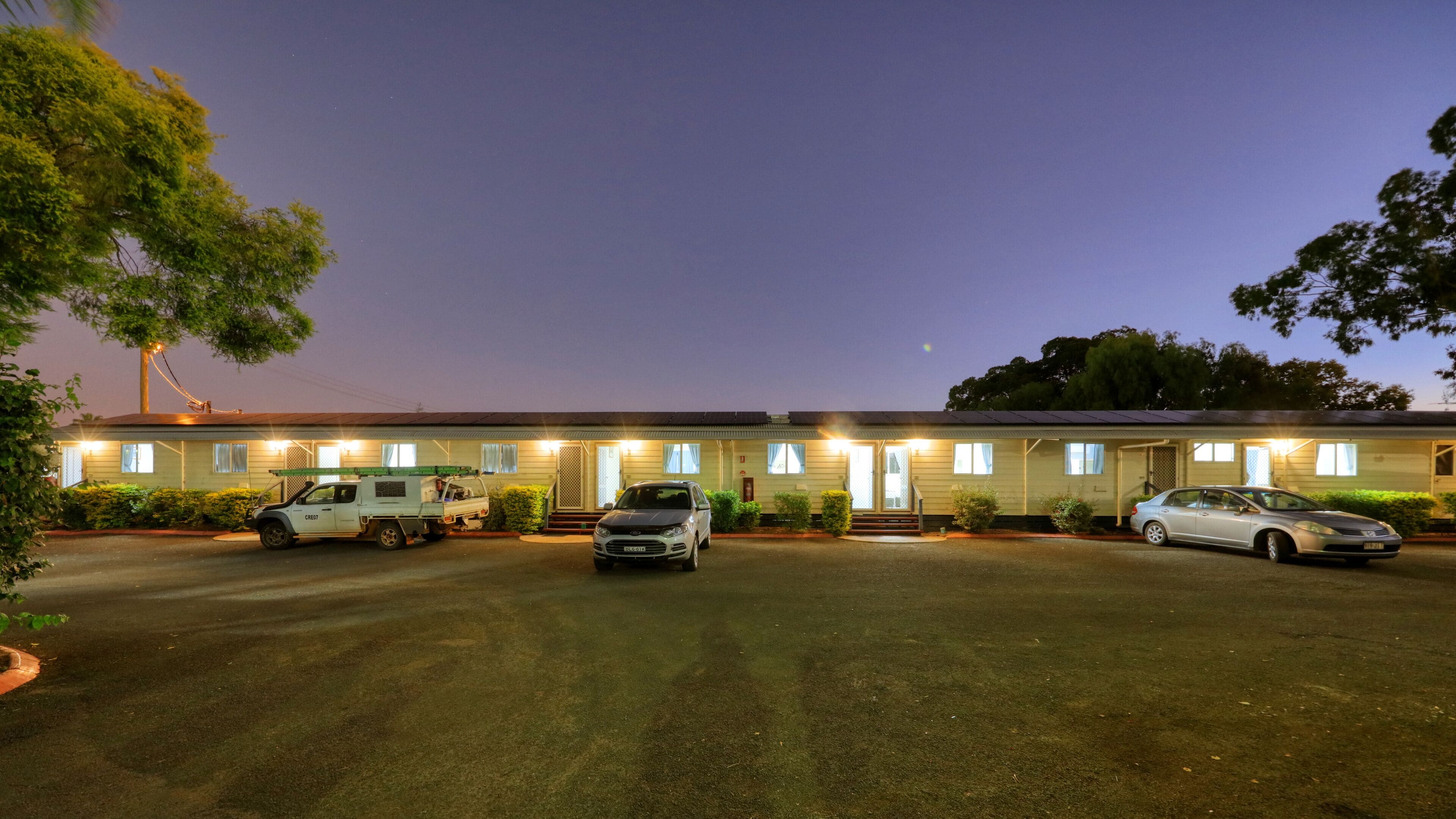 A motel with a row of rooms, a parking lot, and a small building with a sign.