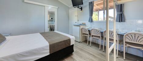 Una habitación con cama, escritorio, sillas, televisión y kitchenette.