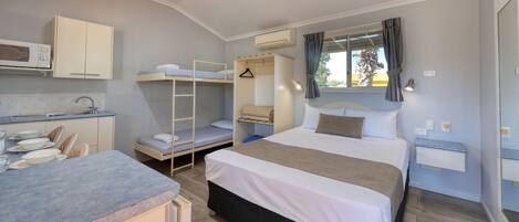 A compact hotel room with a bunk bed, a kitchenette, a single bed, and a window with curtains.