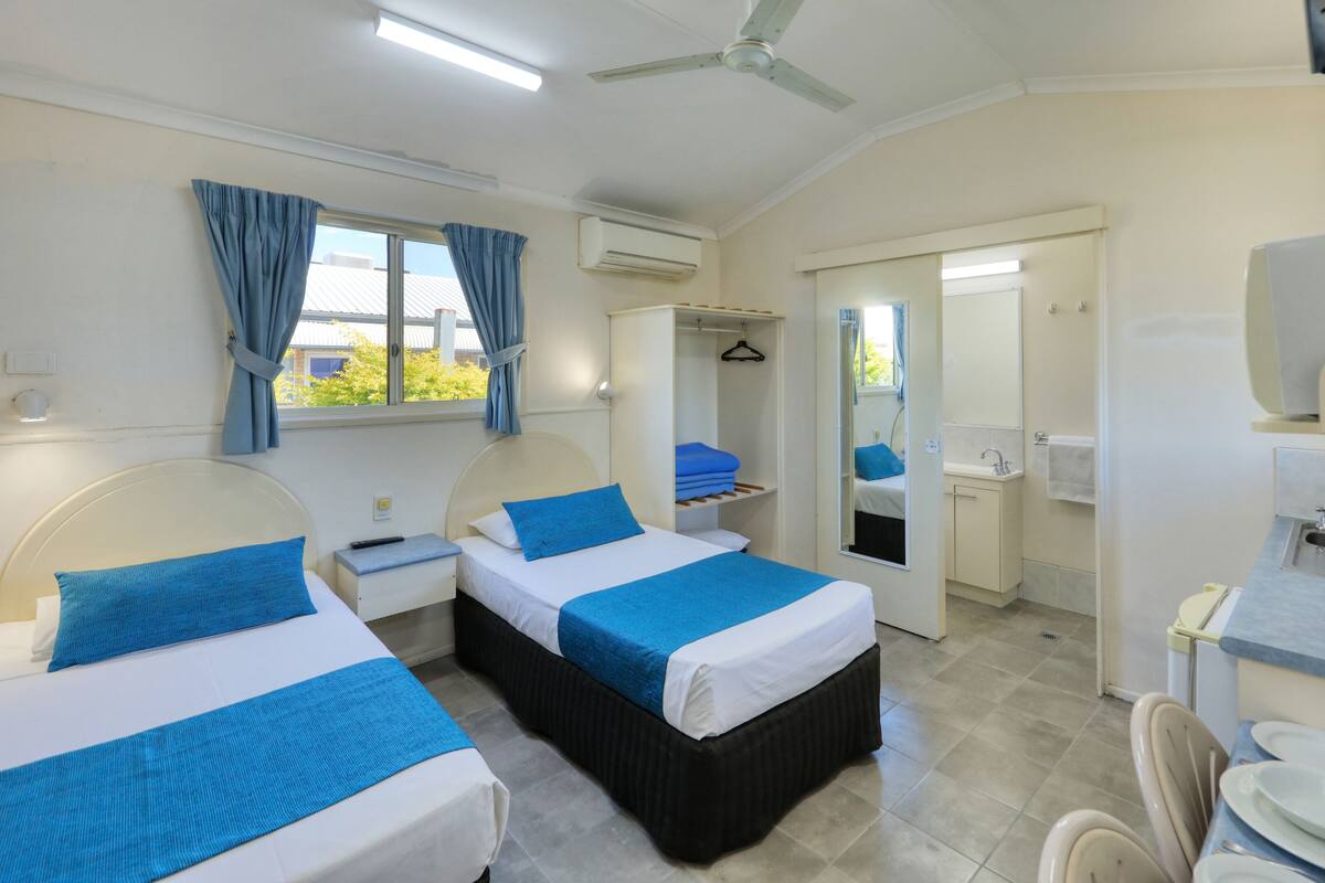 A hotel room with two beds, a bathroom, and a kitchenette.