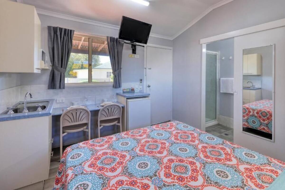 A compact hotel room with a bed, a small desk, a chair, a sink, and a mirror.