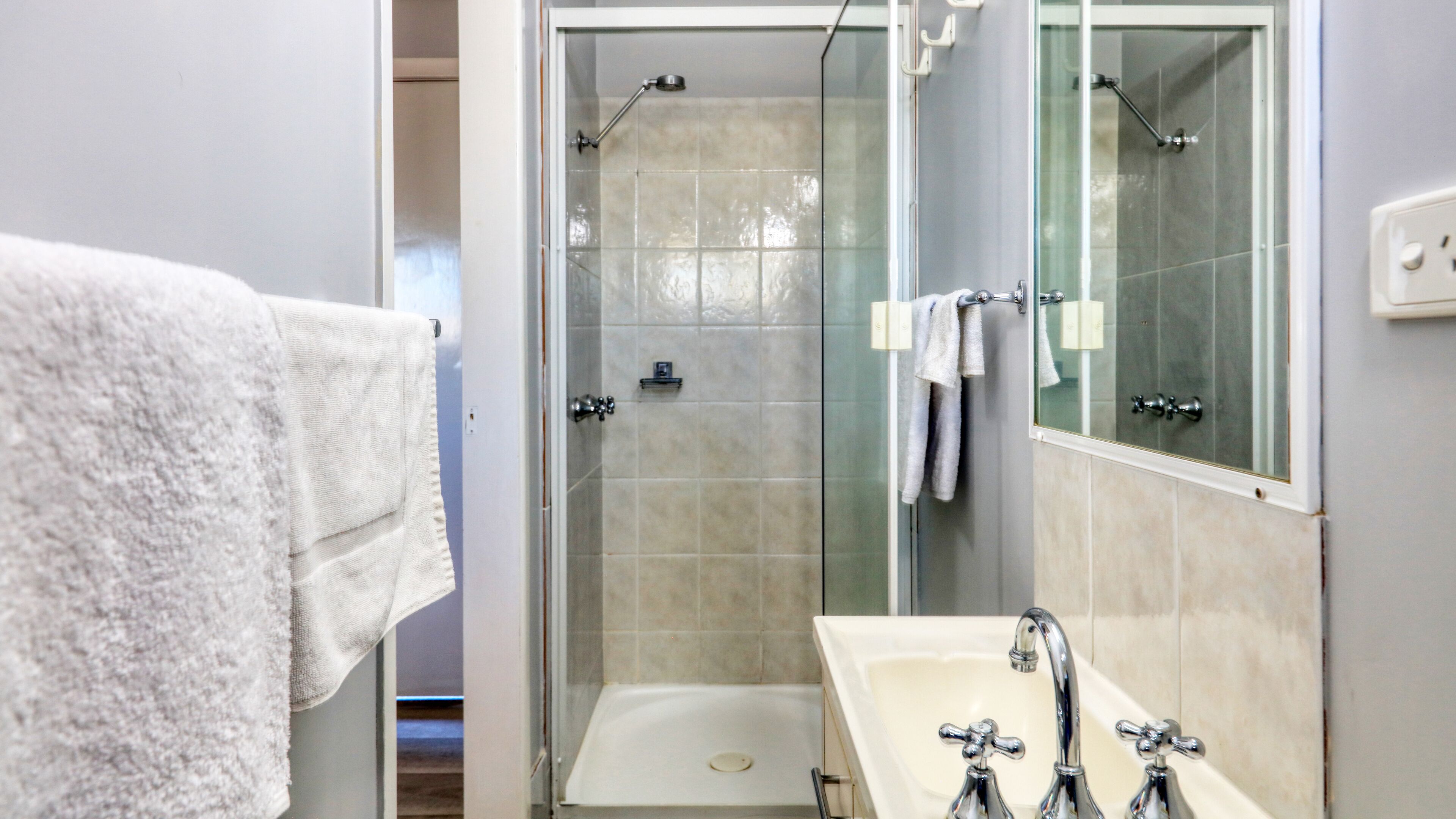 A bathroom with a glass shower enclosure, a white sink, and a mirror.