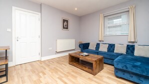 A living room with a blue sofa, a wooden coffee table, a white door, and a window with curtains.