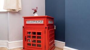 A red telephone booth with the word "TELEPHONE" on it, placed against a blue wall and a white baseboard.