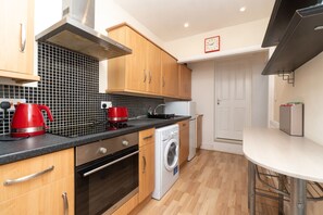 Une cuisine moderne avec des meubles en bois, un crédence en carreaux noirs, une bouilloire rouge, un lave-linge et un réfrigérateur blanc.