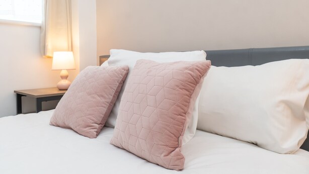 A neatly made bed with two pillows, a bedside lamp, and a window with curtains.